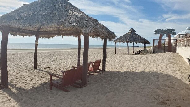 Une plage avec des parasols en chaume et des chaises en bois.