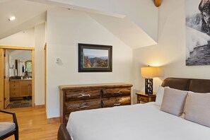 Une chambre à coucher avec un lit, une commode en bois, une table de chevet avec une lampe et un tableau encadré au mur.