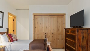 Een slaapkamer met een bed, een houten garderobe, een televisie en een deur.