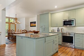 Een moderne keuken met een centraal eiland, roestvrijstalen apparatuur en lichtgroene kastjes.