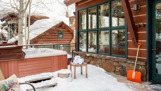 Een sneeuwtbedekte patio met een jacuzzi, een houten bank en een stenen muur.