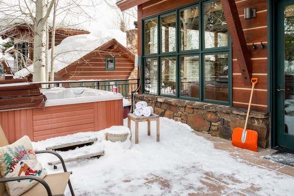 A snow-covered patio with a hot tub, a wooden bench, and a stone wall.