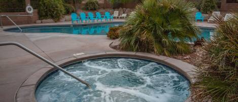 A hot tub with a metal ladder, surrounded by a pool area with blue chairs and palm trees.