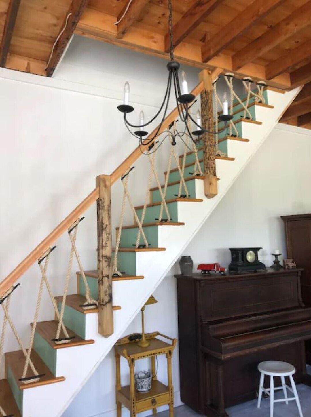 Eine Treppe mit Holzbalken und Seilgeländern, eine Chandelüster und ein Holzkabinett mit einer Uhr.