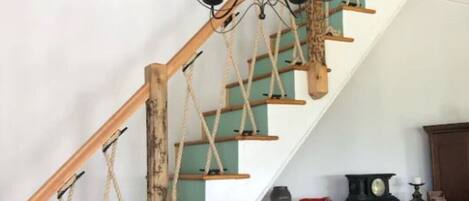 Eine Treppe mit Holzbalken und Seilgeländern, eine Chandelüster und ein Holzkabinett mit einer Uhr.