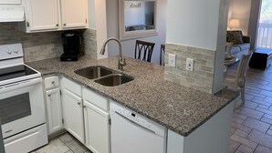 A kitchen with white cabinets, a double sink, a coffee maker, and a dishwasher. - Ocean View Unit 3305 - Ocean & Racquet Resort [20% DISCOUNT ON 7+ NIGHT STAYS] (St. Augustine Beach)