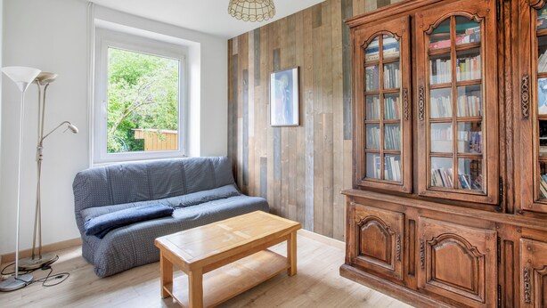 Une pièce avec un plancher en bois, un canapé, un meuble en bois doté de portes en verre et un luminaire suspendu.
