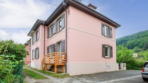 Une maison rose à deux étages, avec un escalier en bois, une clôture verte et un ciel dégagé.