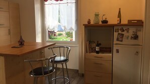 Une cuisine de taille réduite, dotée d’une fenêtre, d’un réfrigérateur et de deux tabourets de bar.