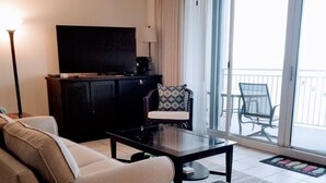 A living room with a sofa, a coffee table with a floral centerpiece, a television, and a ceiling fan. - ☀️ ☀️ BEACH FRONT - BOOKING SPRING & SUMMER - BEACH CHAIR SERVICE INCLD☀️ ☀️ (Panama City Beach)