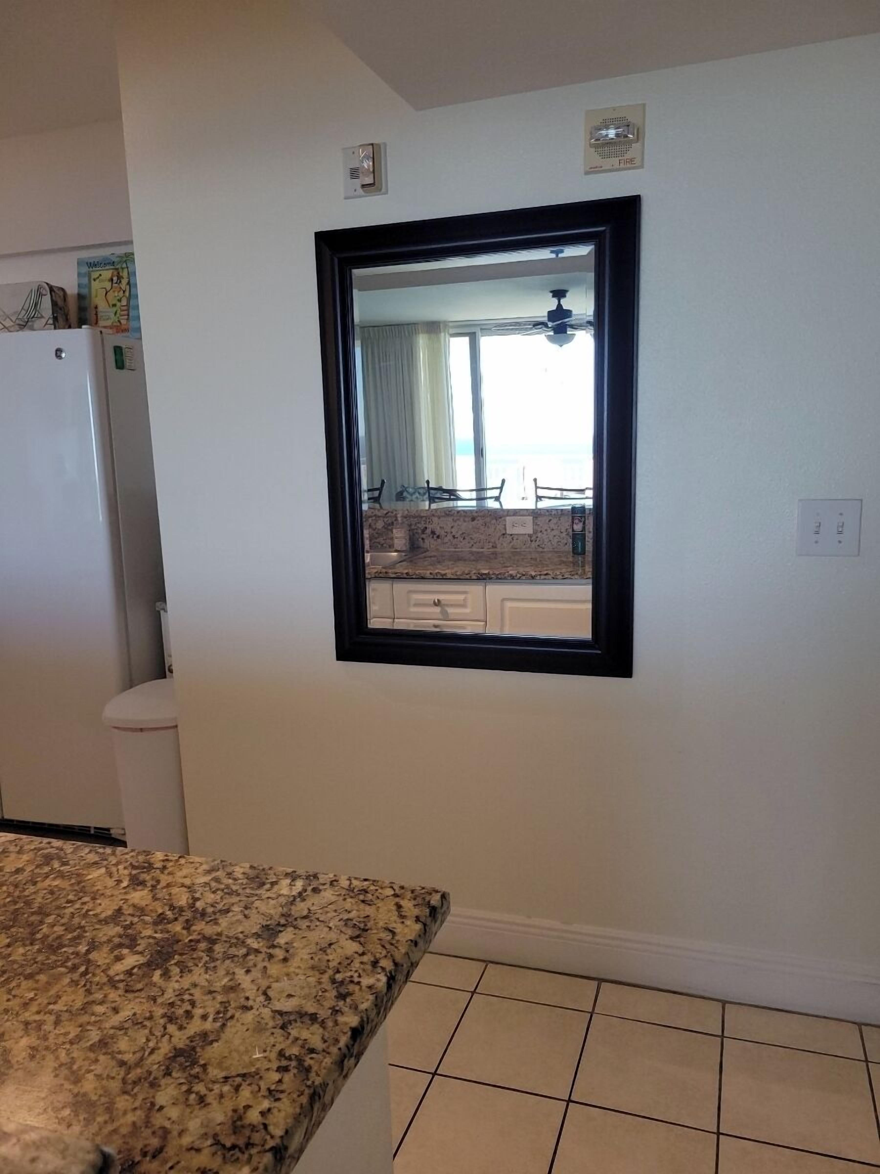 A kitchen with a granite countertop, a white refrigerator, and a window with a view of a balcony.