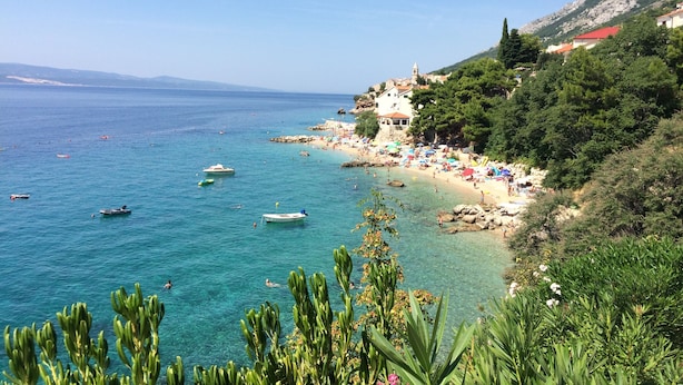 Une scène de plage côtière avec une eau bleue et limpide, des bateaux et un bâtiment doté d’un toit rouge.
