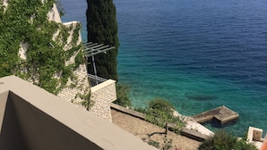 Un balcon avec vue sur la mer, un grand arbre et un mur de pierre.