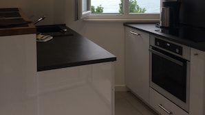 Une cuisine moderne avec vue sur la mer, dotée de meubles blancs, d’un plan de travail noir et d’un four encastré.