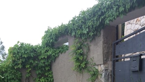 Une terrasse dallée de pierres, avec un bac à plantes en béton et un portail en métal.