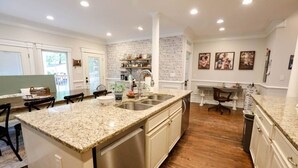 Uma cozinha espaçosa com bancadas de granito, eletrodomésticos de aço inoxidável e parede decorada com tijolos.