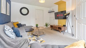 Een moderne woonkamer met een bank, salontafel en een aan de muur bevestigde televisie.