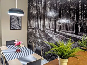 Un coin repas avec une table dressée pour quatre personnes, un luminaire suspendu et une grande fresque murale sur le thème de la forêt.