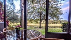 A glass table with wicker chairs and a view of a park with trees and a pond. - Lake View 3BR Condo ...Near Disney and Shopping (Kissimmee)