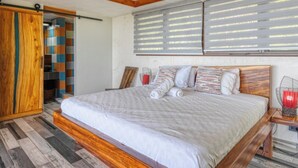 A bedroom with a wooden ceiling fan, a large bed with a wooden frame, and a window with blinds. - Simply Spectacular Luxury Ocean View Villa!  (Uvita)