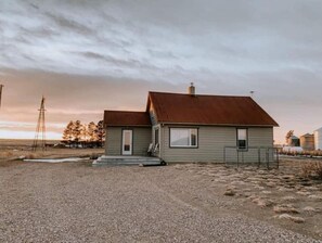 Situated on a rural property, this single-story home features a front porch and a gravel lot with sparse vegetation.