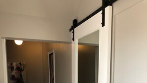 Un pasillo con una puerta corredera estilo granero, un cuadro en la pared y una planta cerca de la puerta.