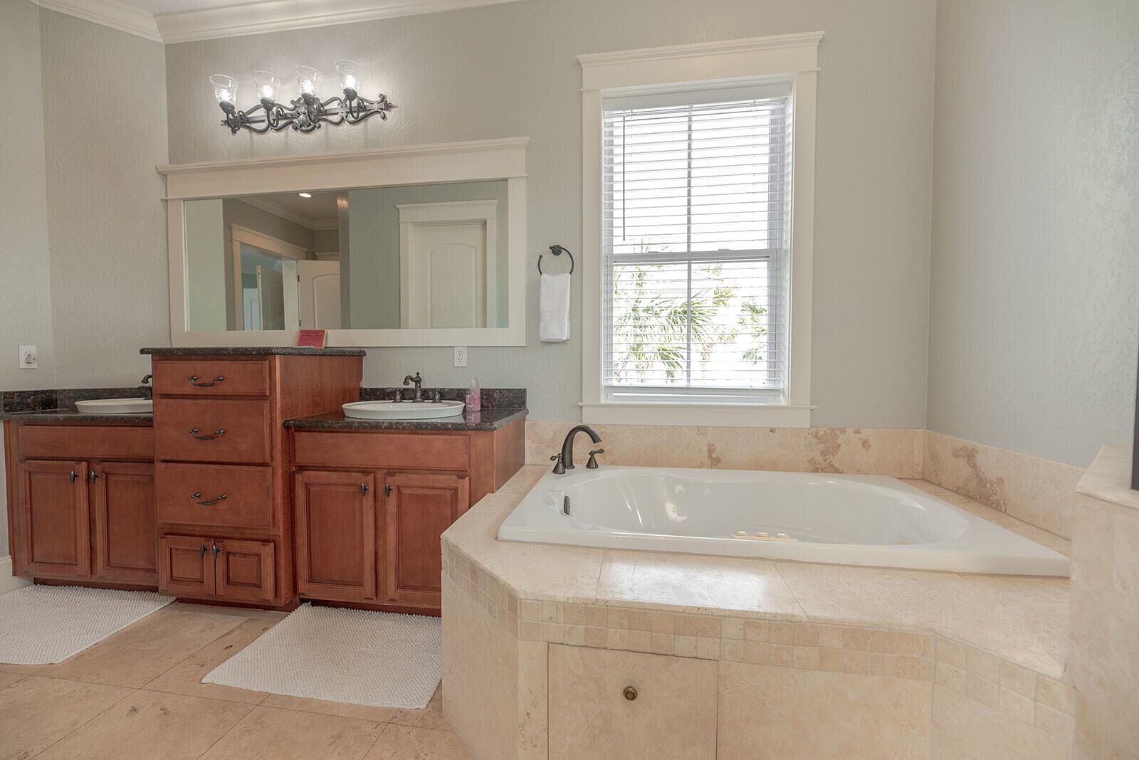A bathroom with a large bathtub, wooden vanity, and a window with blinds.