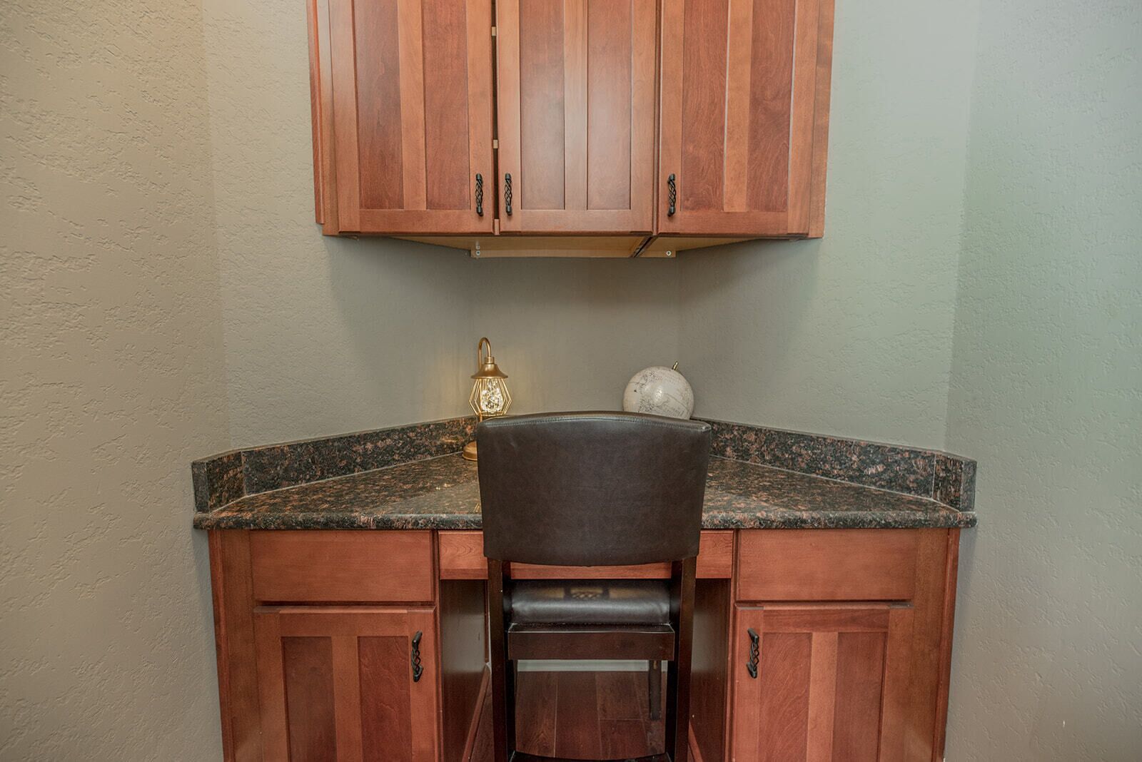 A kitchen with wooden cabinets, a granite countertop, and a chair.