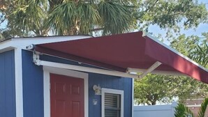 Un petit bâtiment d’un seul étage, avec une porte rouge et une fenêtre, entouré d’une terrasse agrémentée d’une table et de chaises.