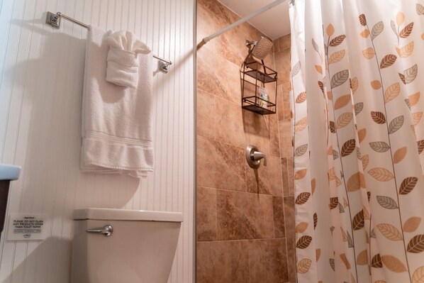 Baño con inodoro, toallero, ducha con repisa metálica y cortina de ducha con diseño de hojas.