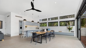 Una cocina moderna con una isla central, taburetes de bar y un comedor con una mesa grande y sillas.