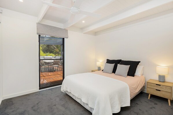 A bedroom with a bed, bedside tables, a nightstand, a ceiling fan, and a sliding glass door leading to an outdoor patio.