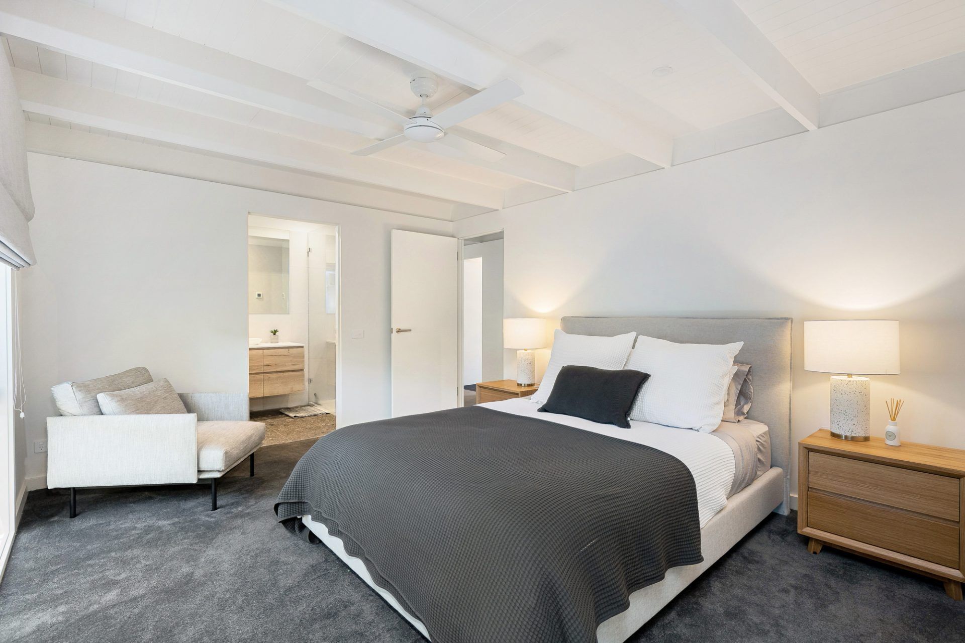 A modern bedroom with a large bed, bedside tables, a chair, and a ceiling fan.