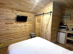 Habitación con paneles de madera, una cama, un televisor, una mesita con microondas y una puerta corredera.