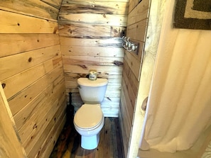 A small, wooden-paneled bathroom with a toilet and a shower curtain.