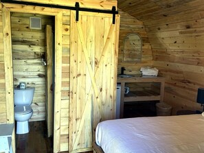 A wooden cabin with a bathroom, a bed, and a small sink area.