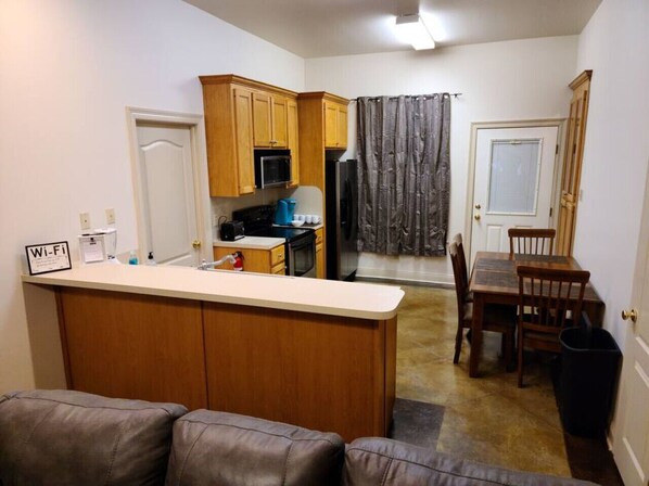 A compact kitchen with wooden cabinets, a microwave, and a refrigerator. There is a dining area with a table and chairs.