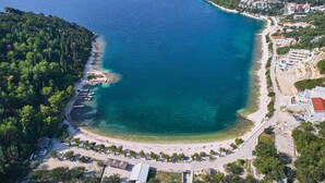 Eine Luftaufnahme einer Küstenregion mit Strand, klarem, blauem Wasser und einem bewaldeten Hügel.