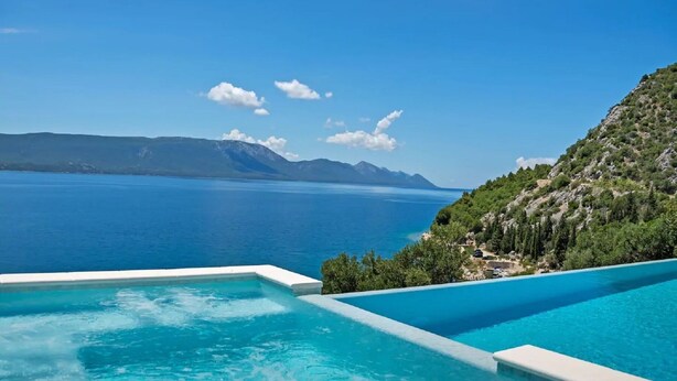 Ein Pool mit freiem Blick auf ein großes Gewässer und entfernte Berge.