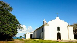 A white church with a cross on top, surrounded by trees and a clear sky. - Estúdio Martinelli (Porto Seguro)