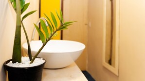 A bathroom with a white sink, a potted plant, and a yellow wall. - Estúdio Martinelli (Porto Seguro)
