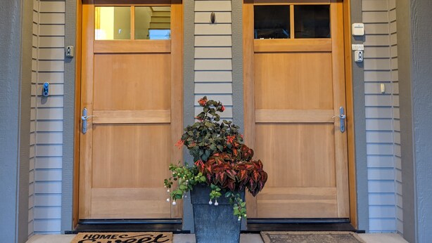 A double wooden door with a small window above each door, a potted plant in front, and a doormat with the word "HOME" on it. - Downtown Loft on Lupfer (Whitefish)