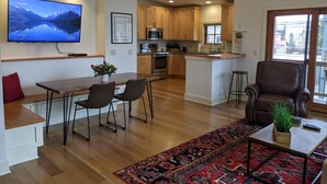 A modern kitchen with wooden cabinets, a central island, and a dining area with a table and chairs. - Downtown Loft on Lupfer (Whitefish)