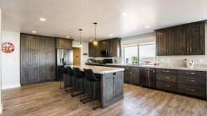 Una cocina moderna con armarios de madera oscura, una isla central con taburetes de bar, electrodomésticos de acero inoxidable y un ventanal con vistas.