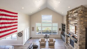 Un salón espacioso con techo alto, chimenea de piedra, ventana grande con vistas al exterior e una bandera en la pared.