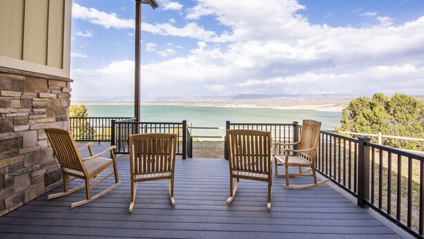 Una terraza de madera con tres mecedoras que da a un cuerpo de agua y montañas distantes.