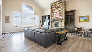 Un salón amplio con chimenea de piedra, un sofá seccional gris grande y un comedor con mesa y sillas de madera.