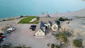 Una casa grande con un amplio camino de entrada y un pequeño jardín, ubicada cerca de una gran extensión de agua y una playa.