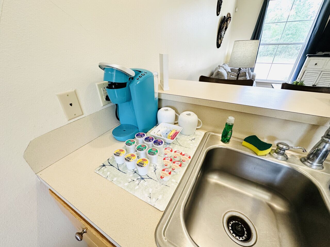 Une cuisine équipée d’un évier, d’une cafetière bleue et de divers aliments disposés sur le plan de travail.