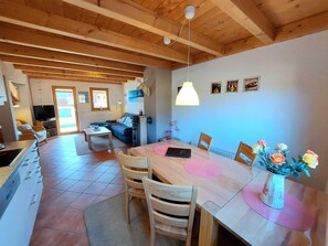 A spacious living area with a wooden ceiling, a dining table with chairs, a sofa, and a television in the background. - A beautiful, comfortable, and pleasant vacation home on the shores of Lake Lechsee, right on the edge of the forest (Lechbruck am See)